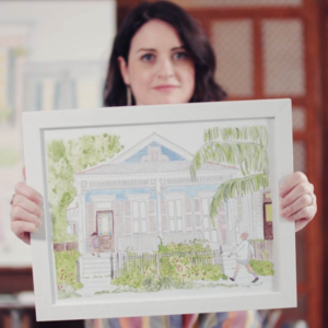 Illustrator, WalkingMan, behind her illustration of a New Orleans house.